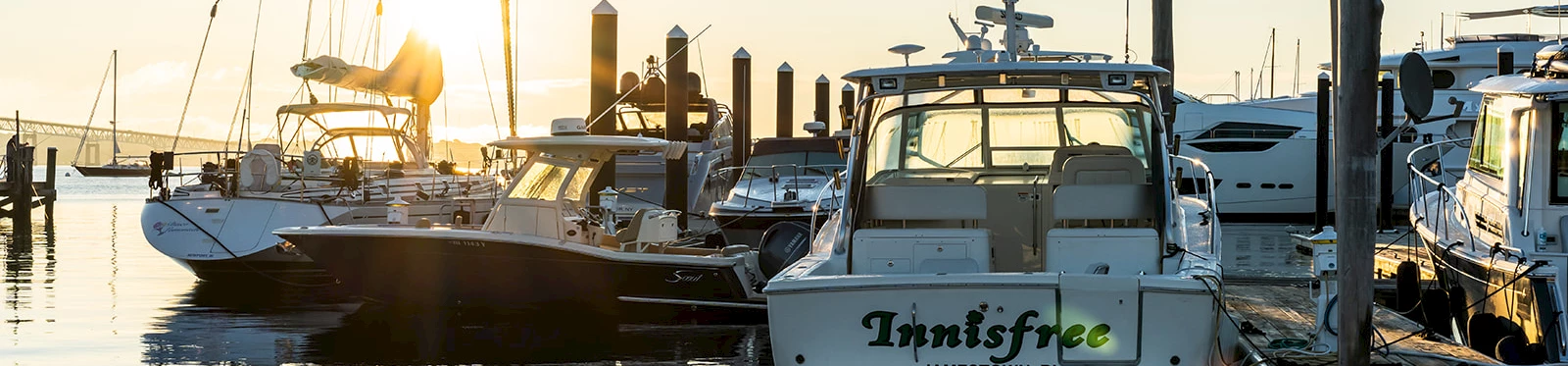 Boats docked at a marina during sunset with reflections on the water.